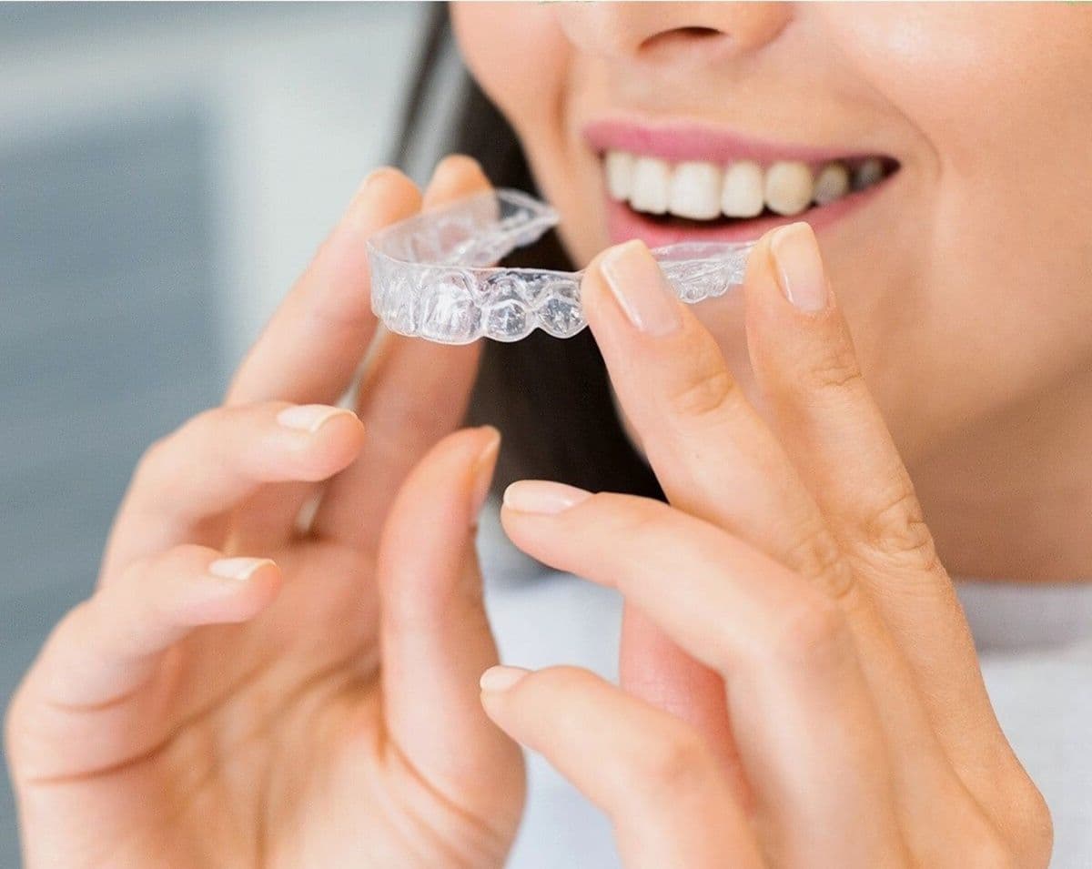 A clear aligner tray held up to a bright, healthy smile